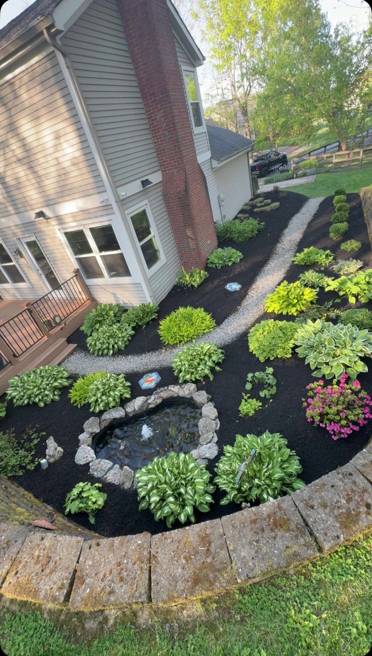 Finished residential garden bed with pond, plantings, mulch, and stone border